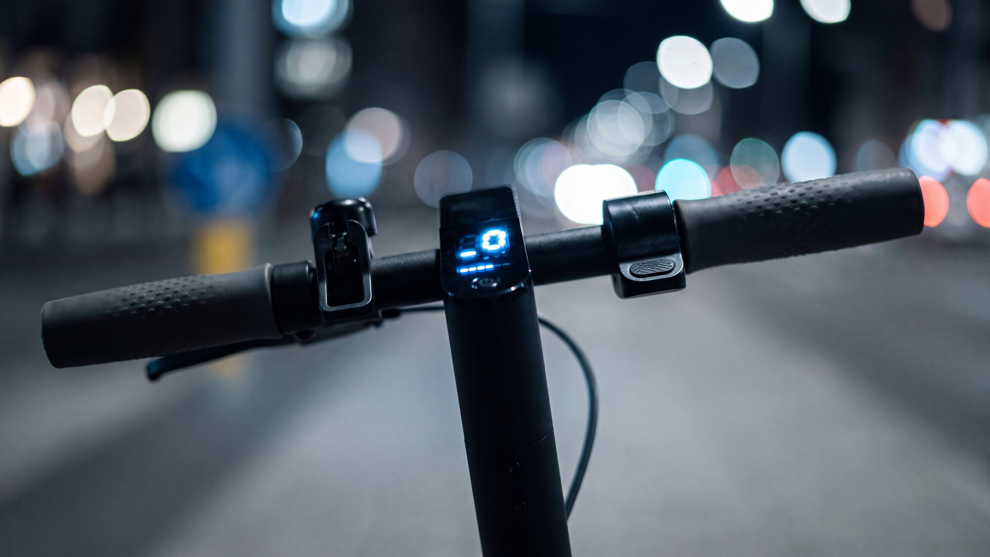 Fotografia serale ravvicinata del manubrio di un monopattino elettrico: il display acceso con la velocità e l'indicatore della batteria
